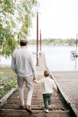 Four sequential images showing parent and child walking together on a wooden dock by a peaceful lake on an autumn day.