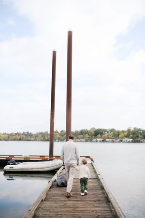 A wooden pier extends into a calm lake on a cloudy day, with distant trees and boats visible along the shoreline.