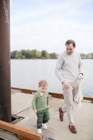 Two people walk together along a waterfront pier with a lake and trees visible in the background.