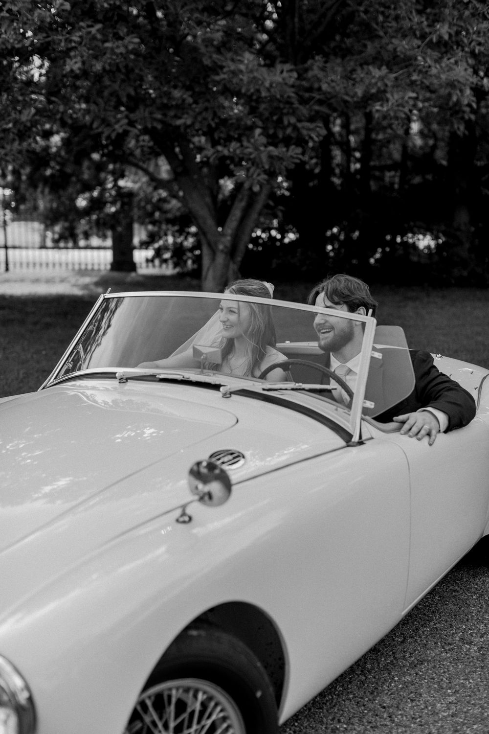 A couple shares a joyful moment in a classic white convertible sports car on a sunny afternoon.