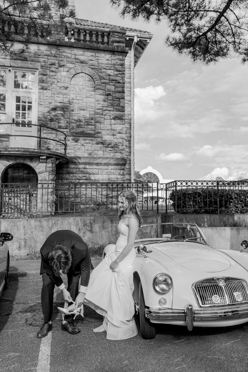 Black and white photograph of a vintage MG sports car parked in front of a stone building.