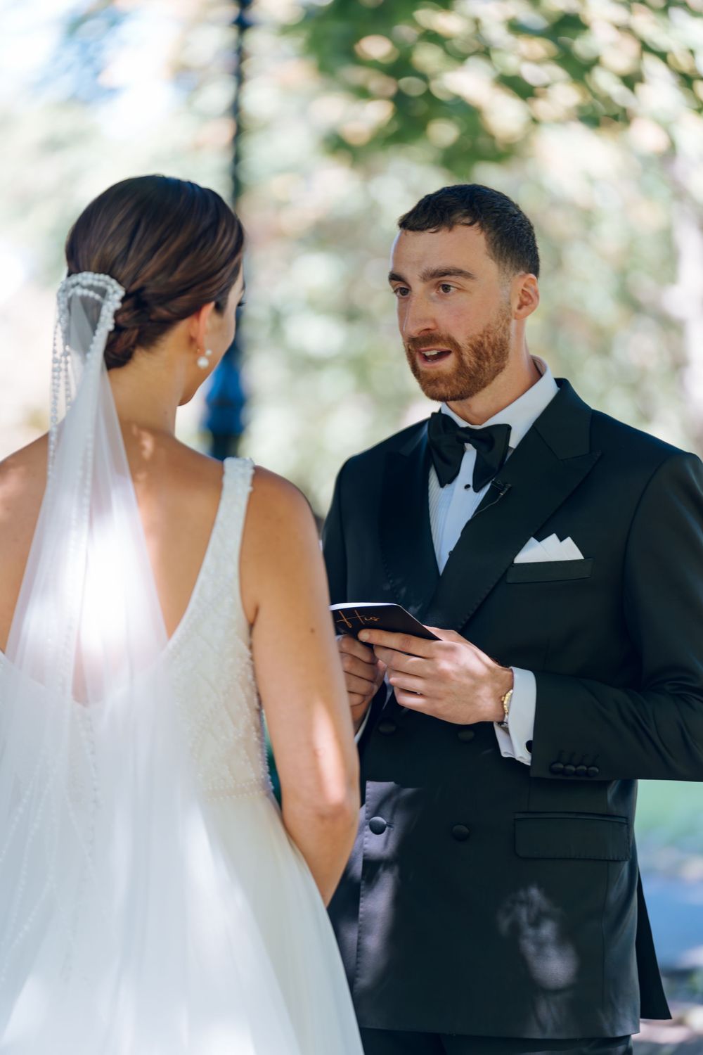 A couple exchanges vows during their outdoor wedding ceremony with the groom reading from a card.