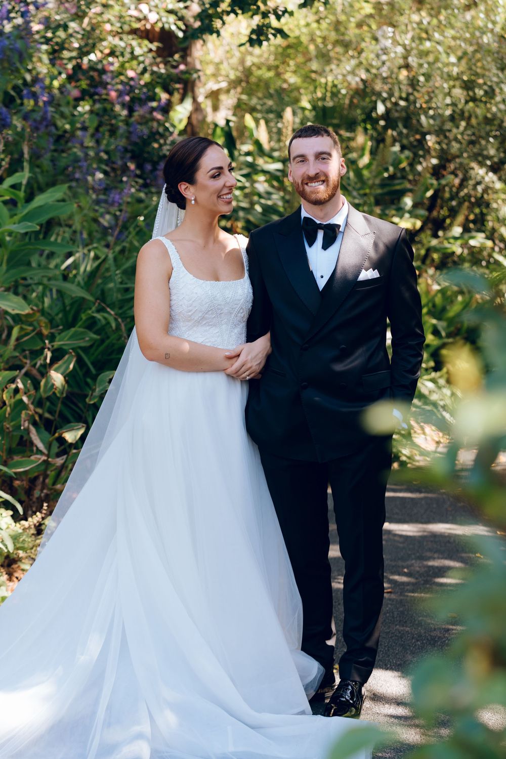 A wedding couple poses together in a lush garden setting with natural greenery in the background.