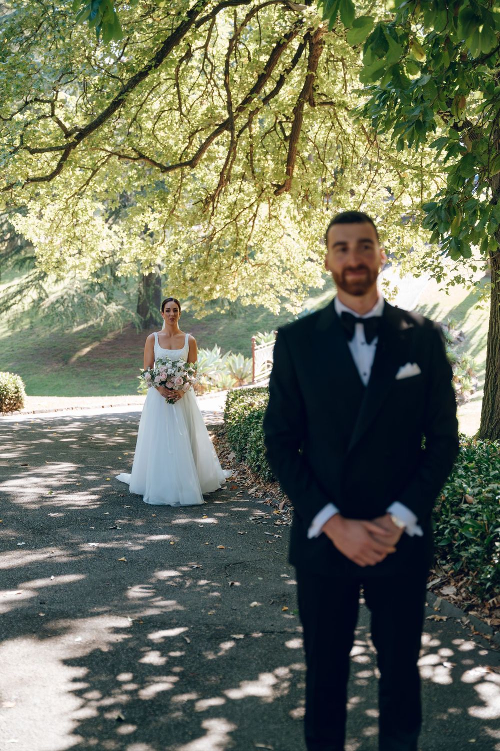 First look wedding moment captured on a tree-lined path.