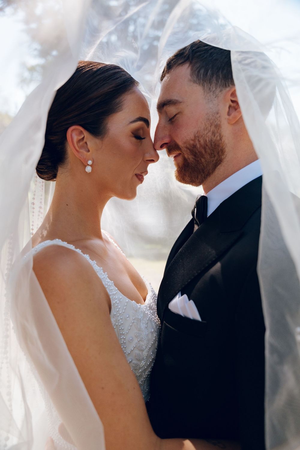 Intimate wedding portrait under a delicate veil with soft lighting.