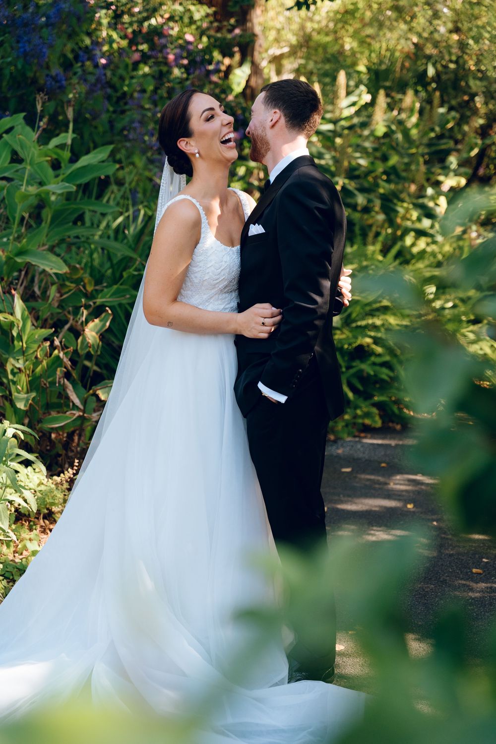 A joyful couple shares a romantic moment in their wedding attire surrounded by lush garden greenery.