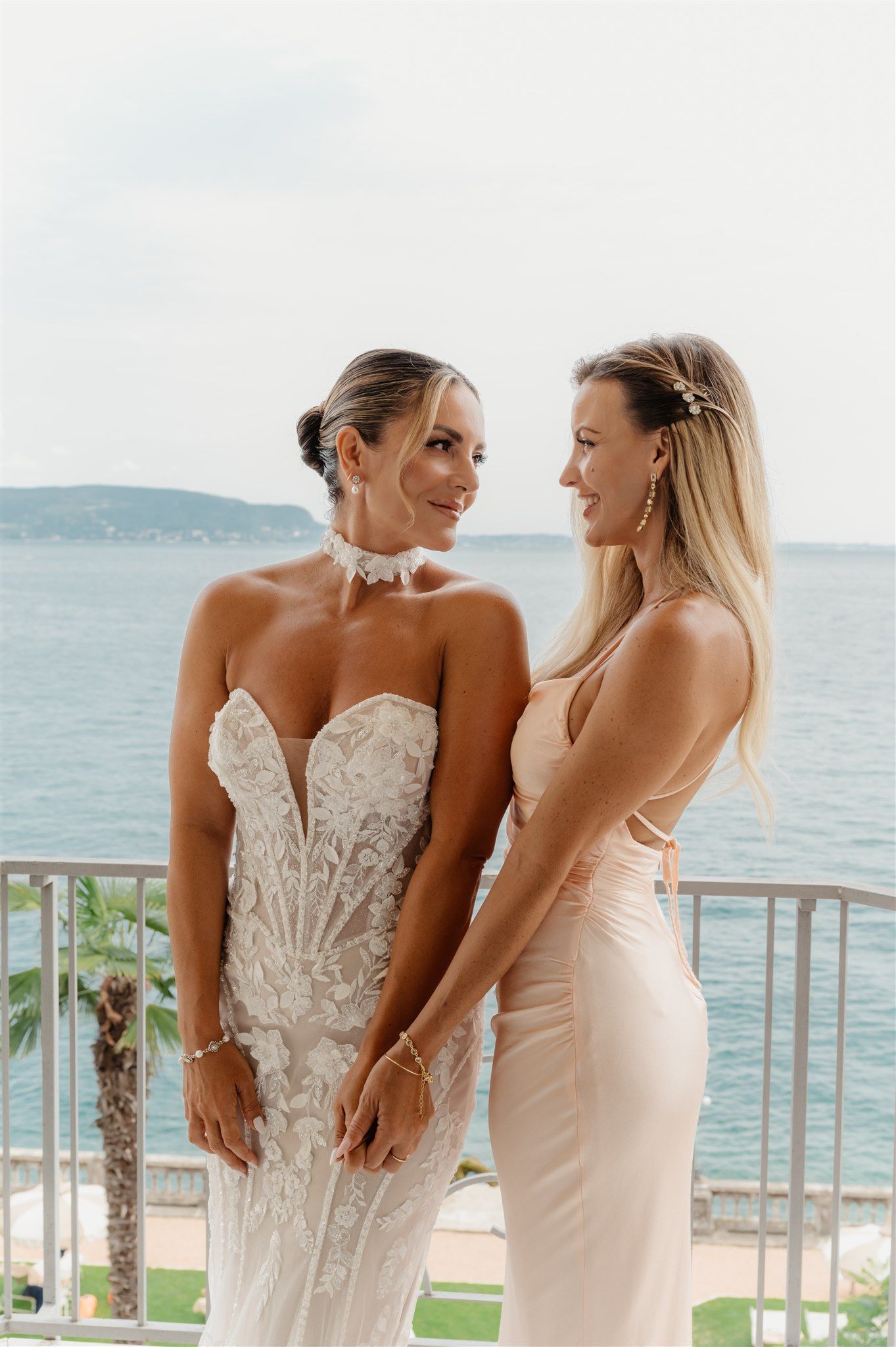 Two elegant white dresses photographed against a scenic lakeside backdrop.