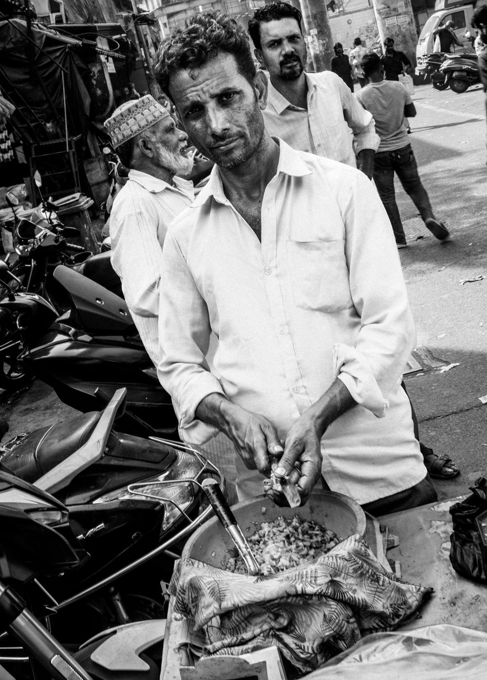 A street vendor in a white shirt prepares food at an outdoor market stall.