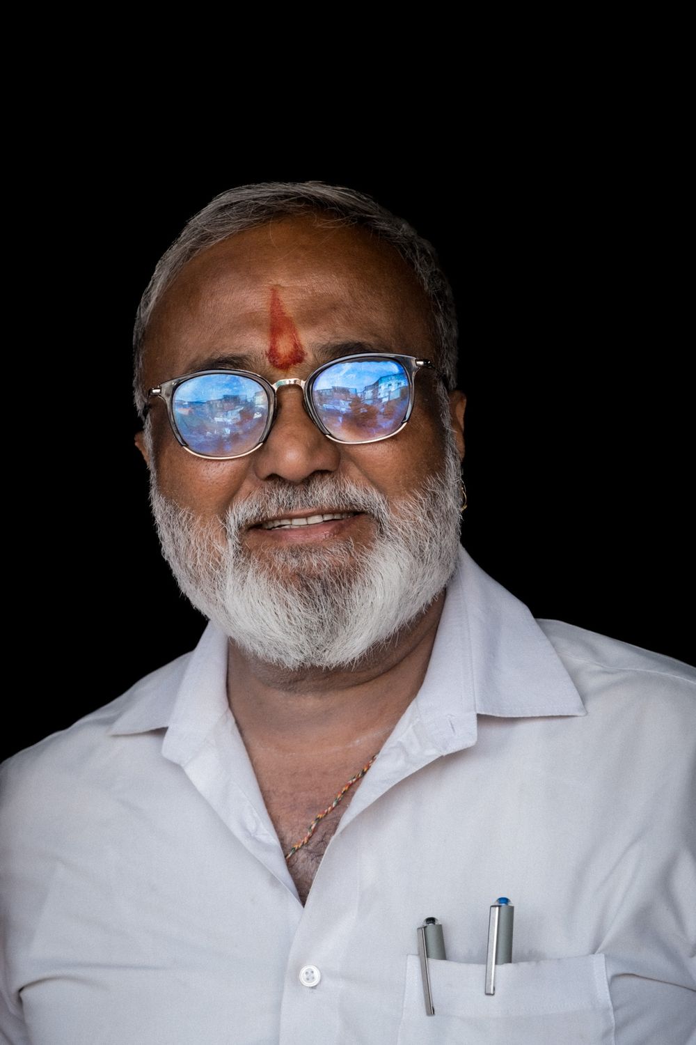 Portrait of an elderly Indian man with glasses and tilak mark on forehead.