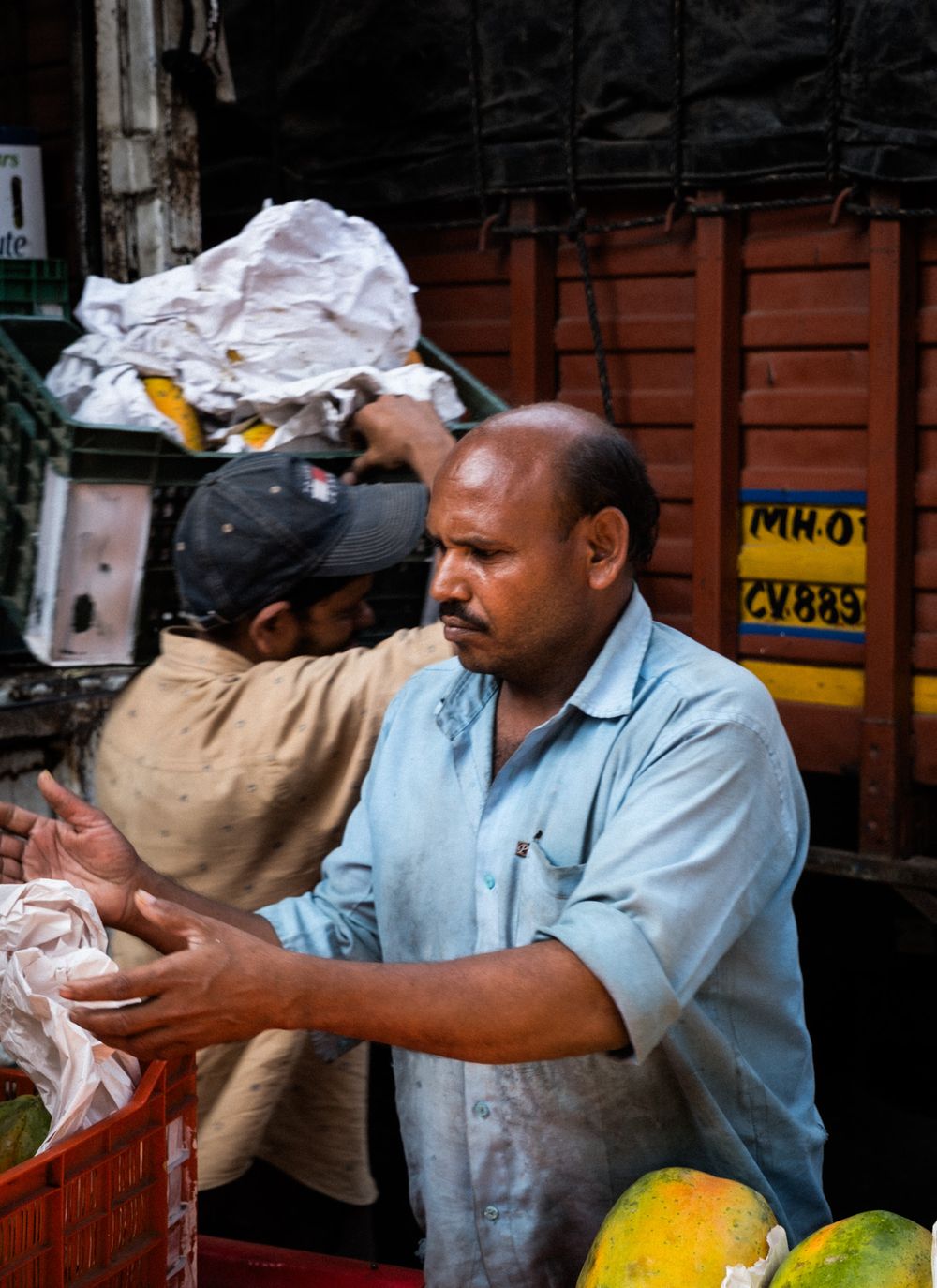 Two men handling goods near a truck at a busy outdoor market.
