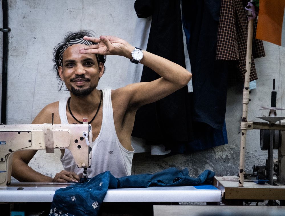 A young tailor in a tank top smiles while working at a sewing machine.