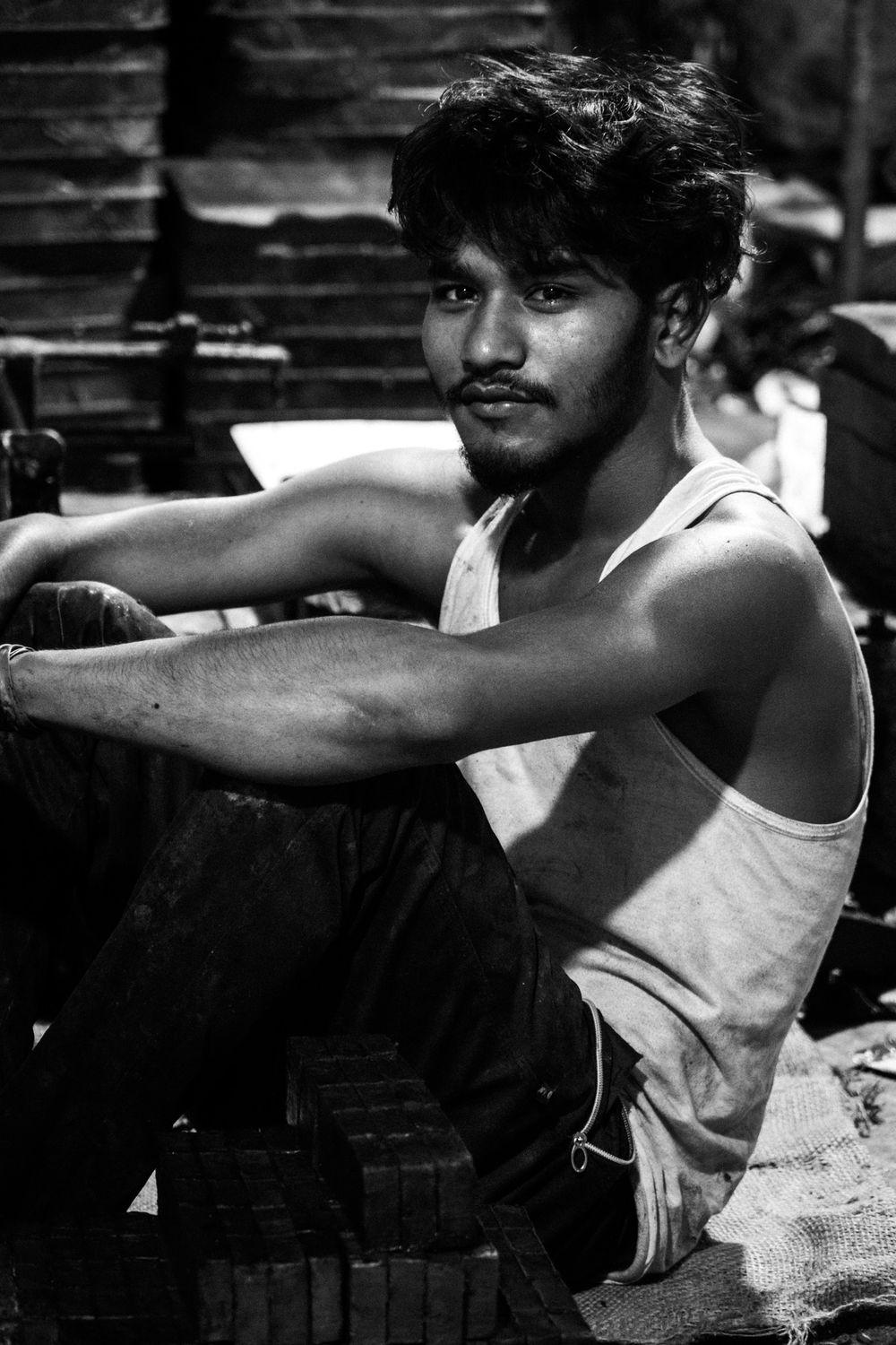 A young Indian laborer in a white tank top rests in a black and white portrait.