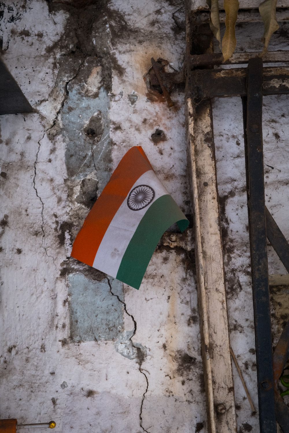 Indian tricolor flag mounted on a cracked weathered white wall with wooden beams.