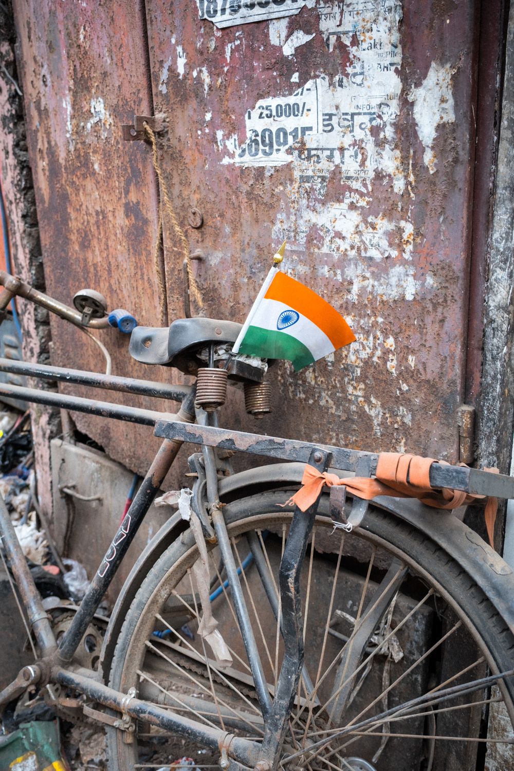 Vintage rusty bicycle with Indian tricolor flag leaning against worn metal door.