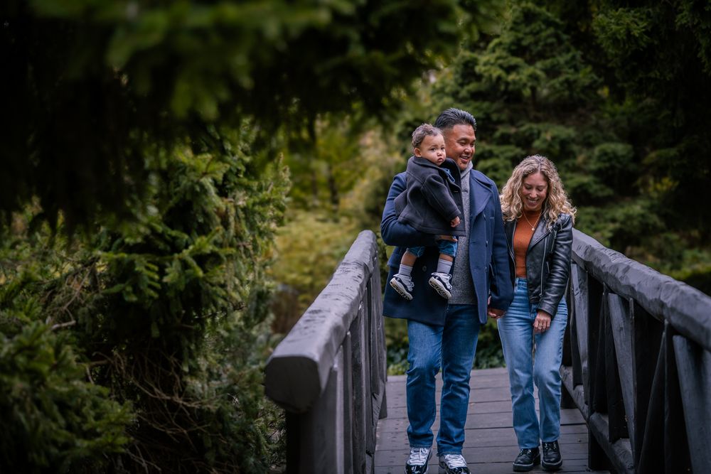 People walking across a scenic wooden footbridge surrounded by lush green forest on a summer day.