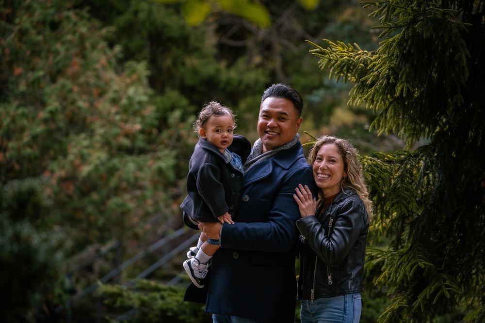 A happy family laughs together during an outdoor photo session in a lush green garden setting.