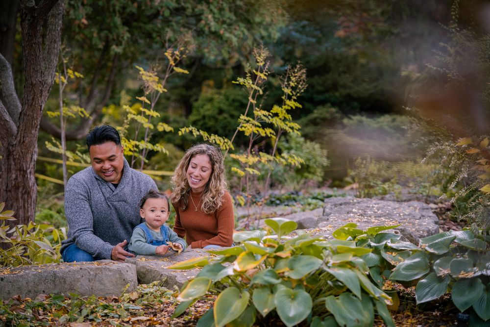 A couple and child pose for autumn family photos in a scenic outdoor setting with fallen leaves.