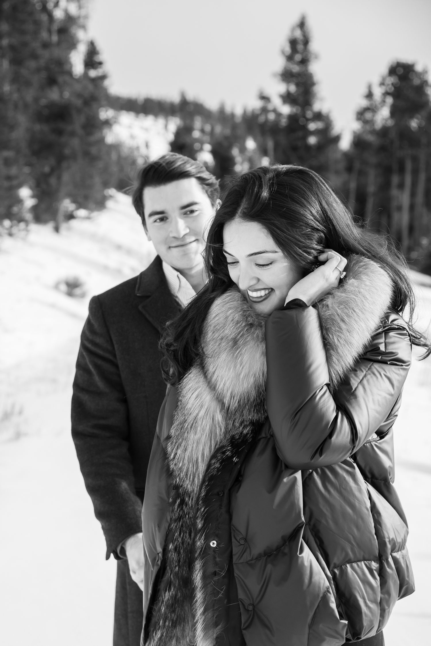 A romantic black and white winter scene with a couple in warm coats standing together in a snowy forest setting in Breckenridge Colorado.