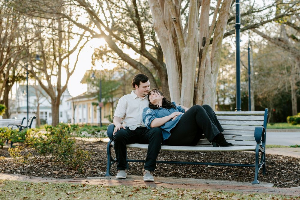 A couple sits together on a blue park bench at sunset with trees and gardens in the background.