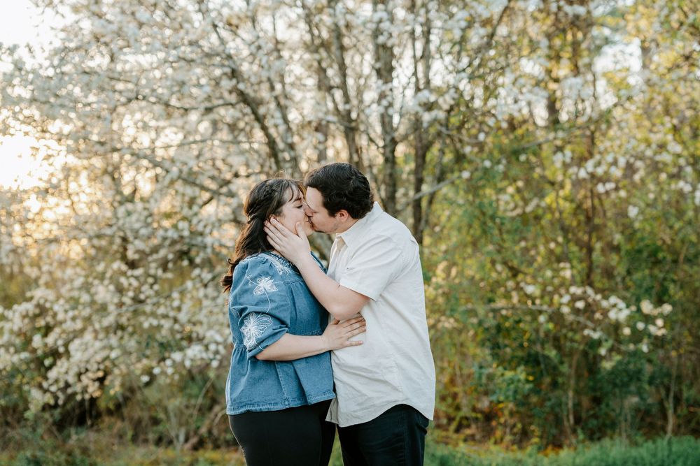 A romantic couple embraces in a sunlit garden with blooming white spring blossoms in the background.
