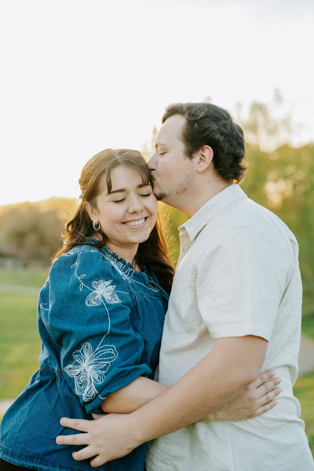 A romantic outdoor portrait of a couple embracing in a field during golden hour, with a butterfly design on denim clothing.