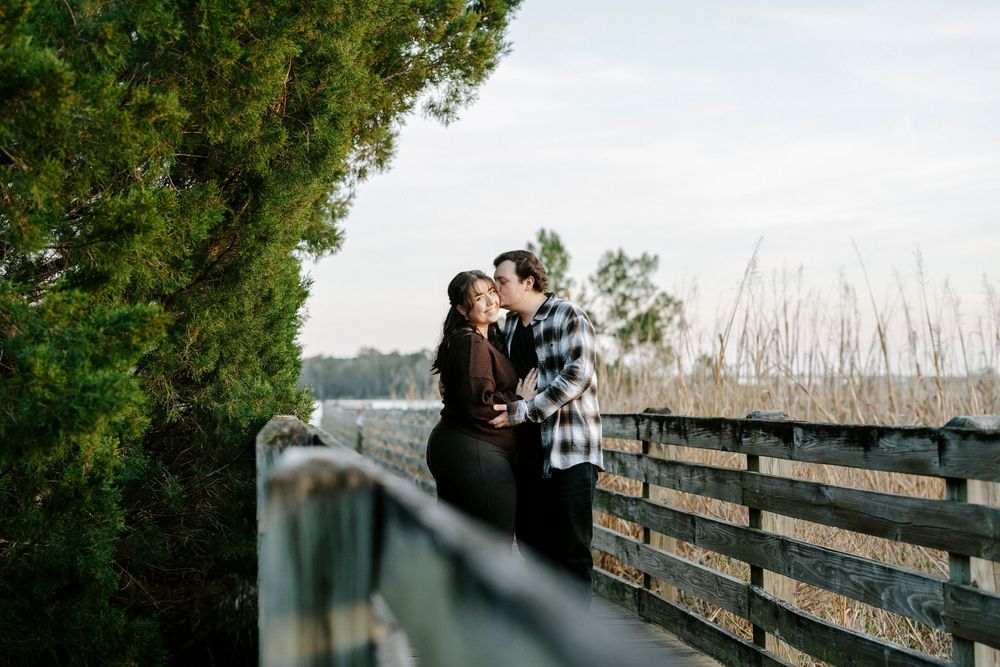 A couple shares a romantic moment on a wooden bridge surrounded by trees during a misty autumn day.