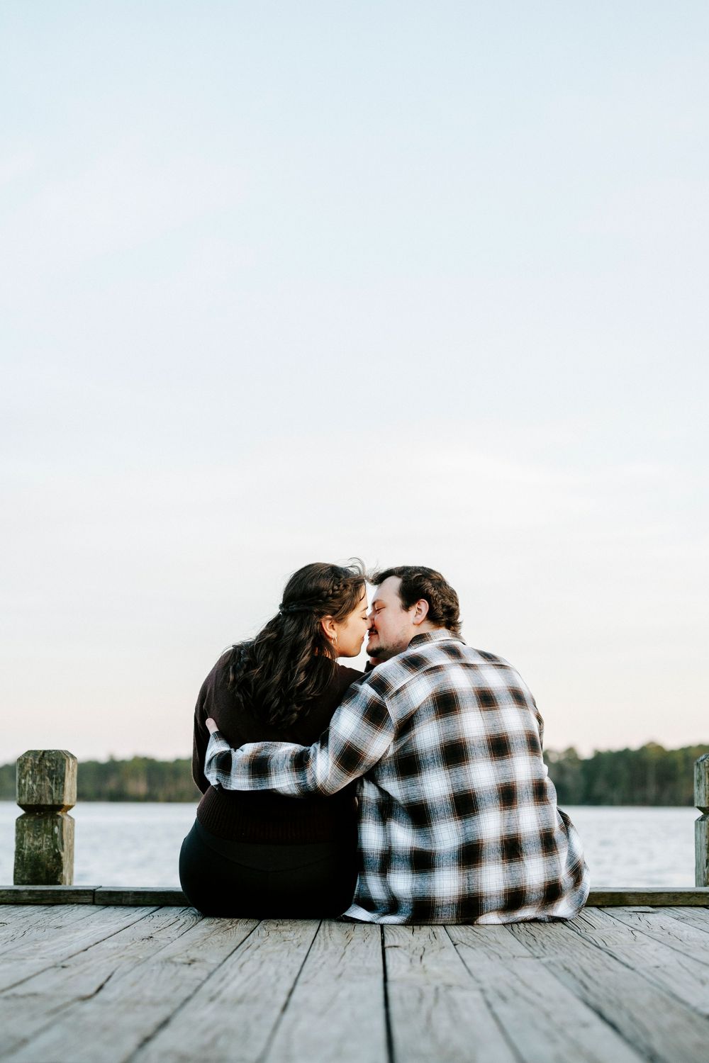 Couple sitting close together on a wooden dock by the water at sunset sharing an intimate moment.