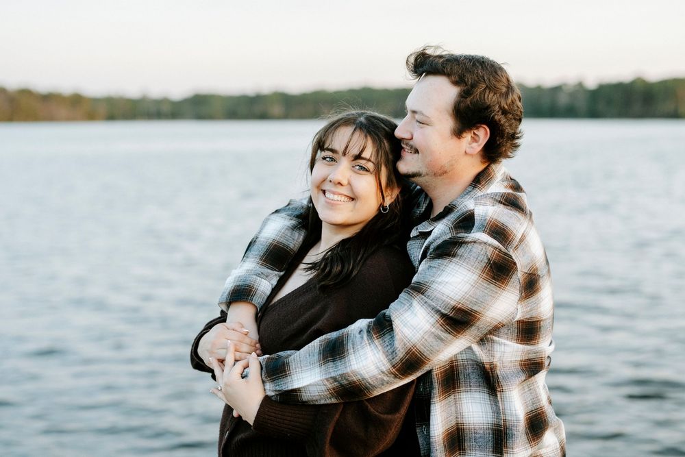 A couple shares a romantic embrace while standing by a lake on an autumn afternoon.