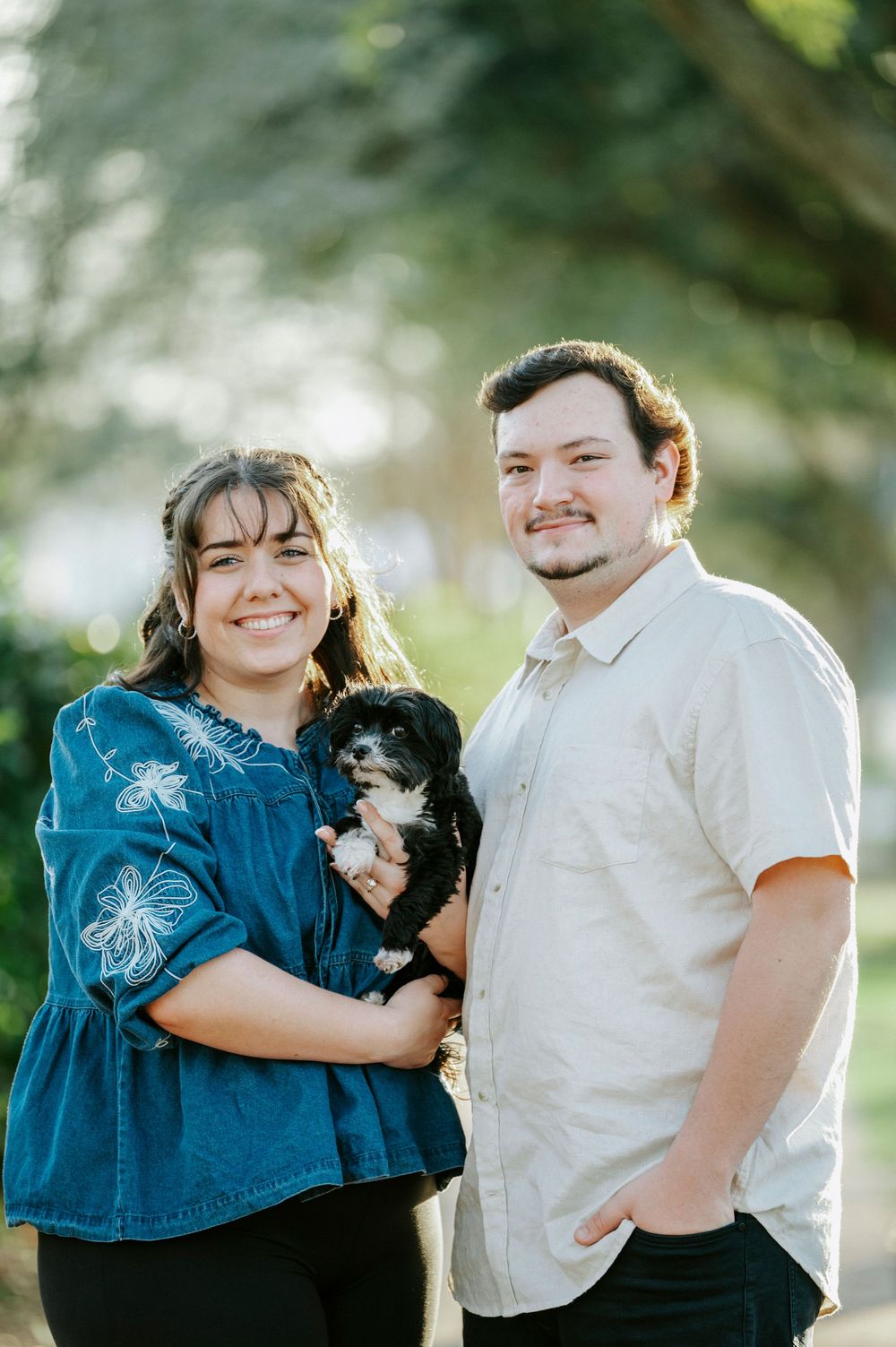 A couple in casual attire sharing tender moments outdoors with their small black dog in a series of photos.