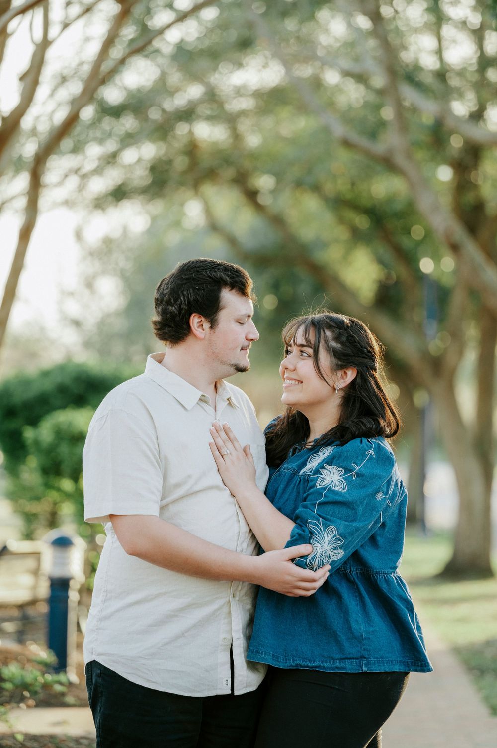 A couple laughs together while embracing outdoors, one in a white shirt and one in blue denim.