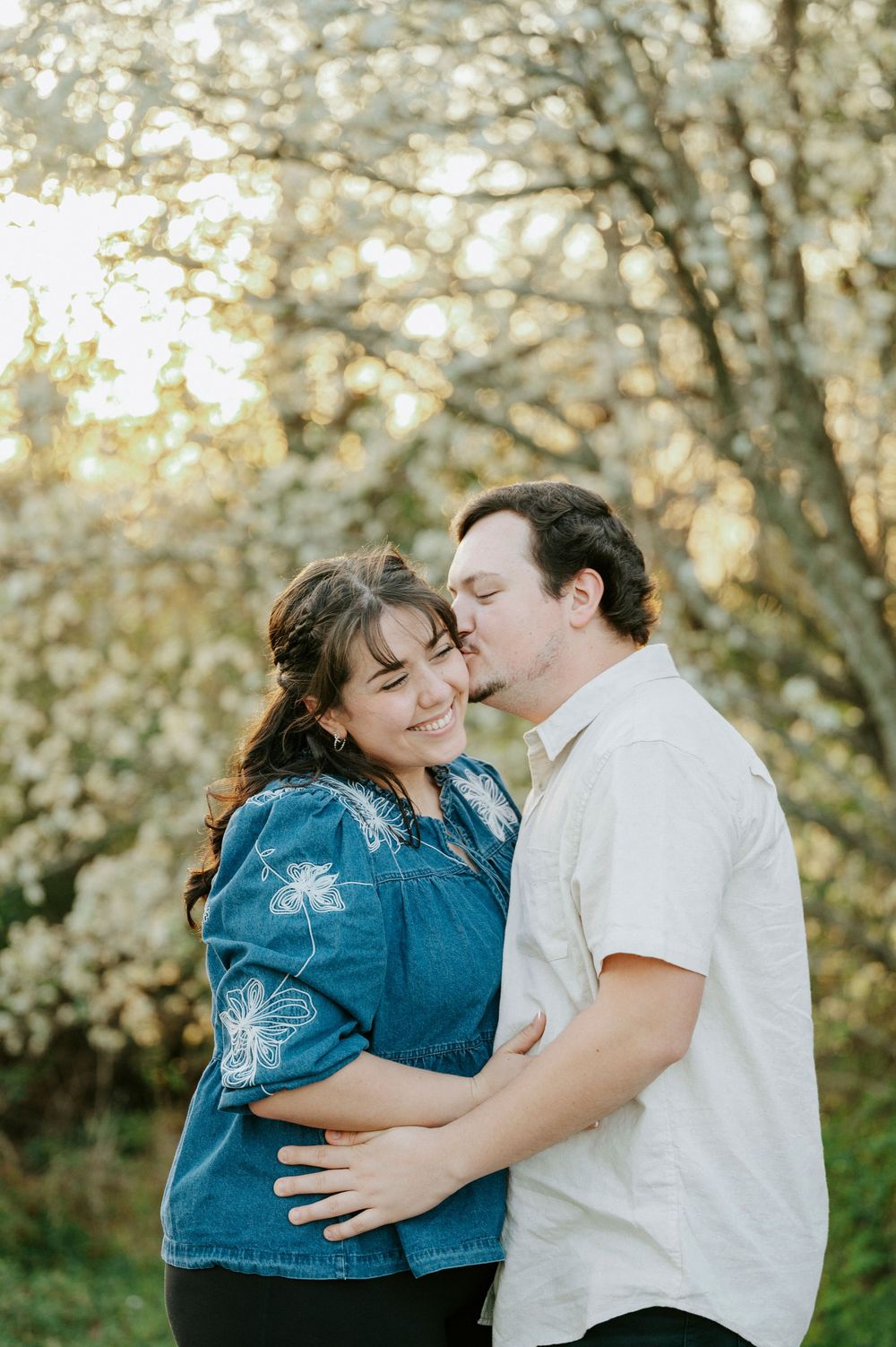 A couple shares joyful embraces among blooming spring trees during a romantic photoshoot.