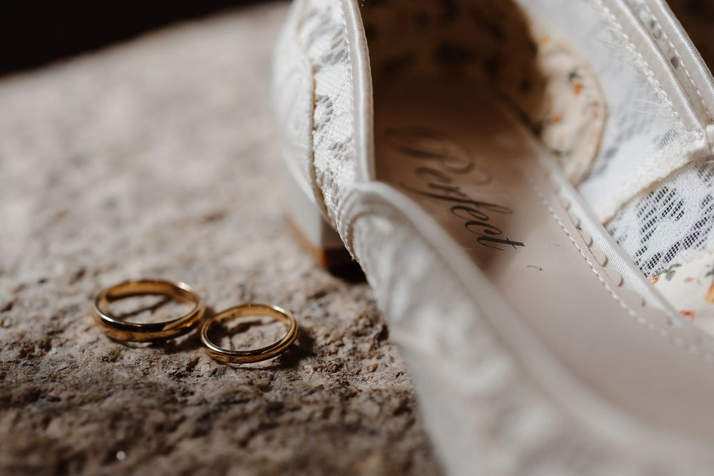 Two wedding rings placed next to a white bridal shoe.