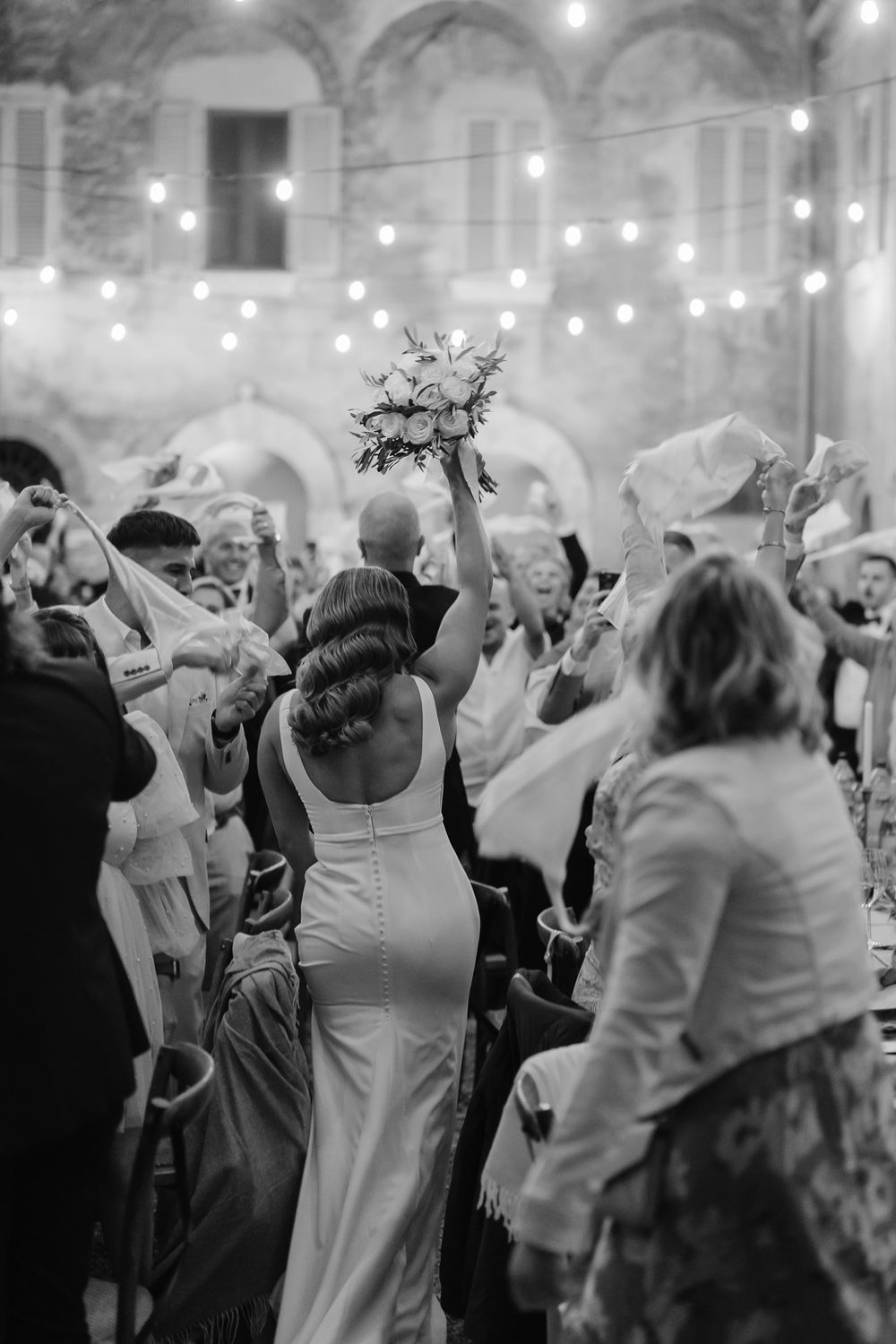 Wedding reception dance party under string lights in historic stone venue.