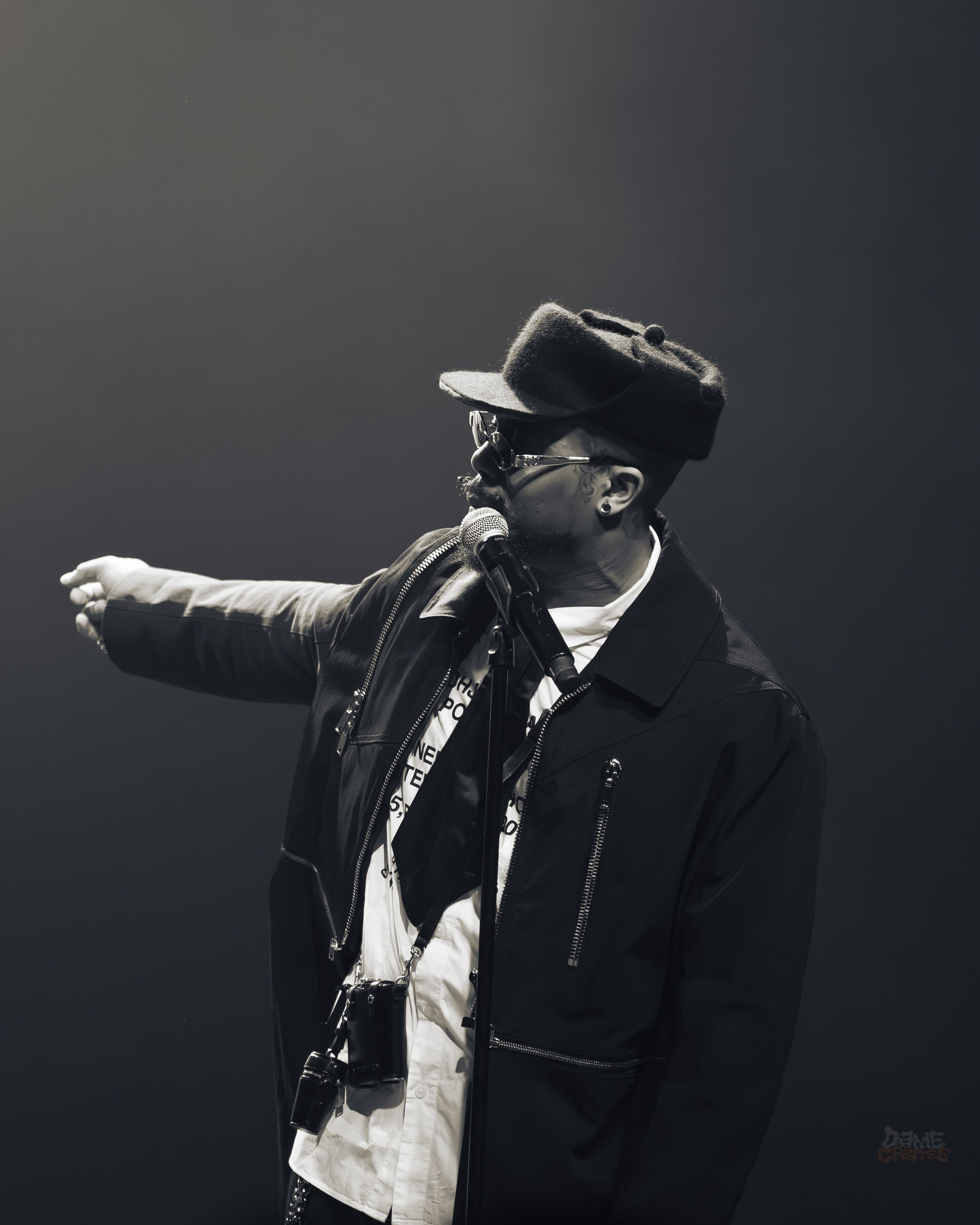 A performer in a dark suit gestures dramatically during a black and white stage performance.