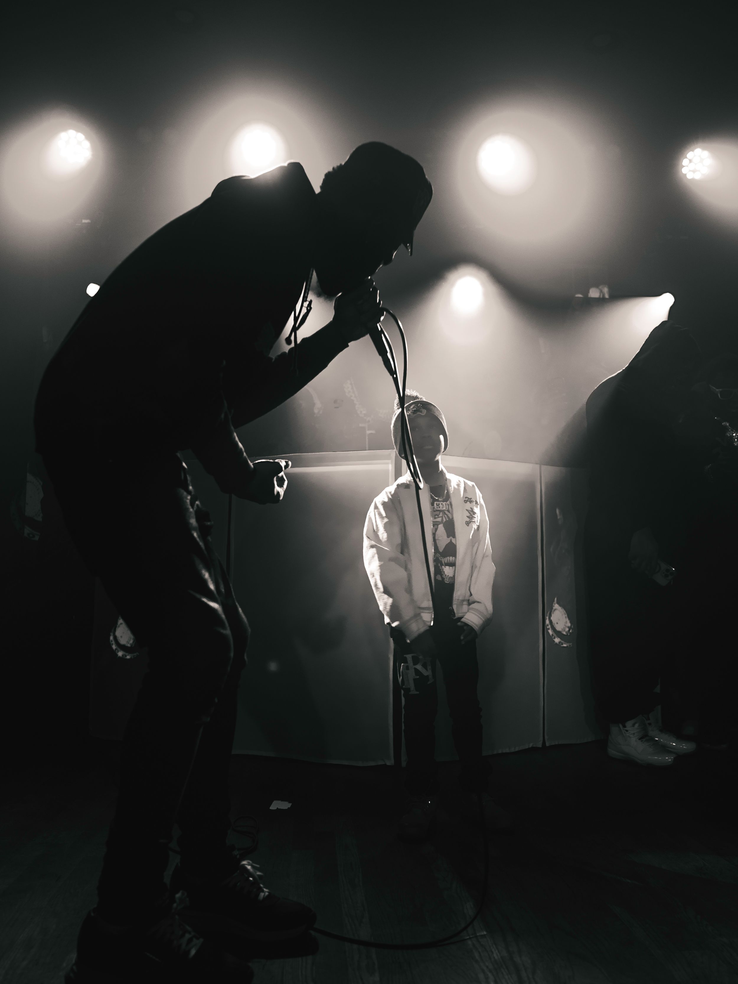 Silhouetted performers on a dimly lit stage with dramatic backlighting creating a moody atmospheric effect.