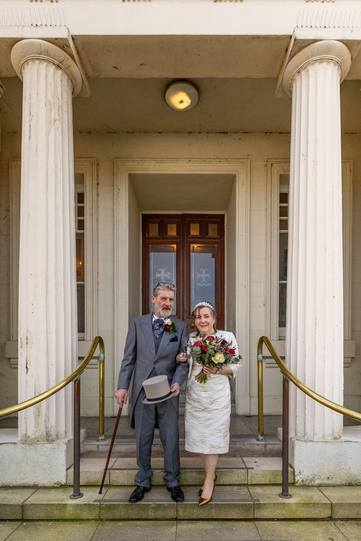 Newlyweds stand arm in arm down the steps of Southport Town Hall, bouquet and top hat in hand, Southport wedding