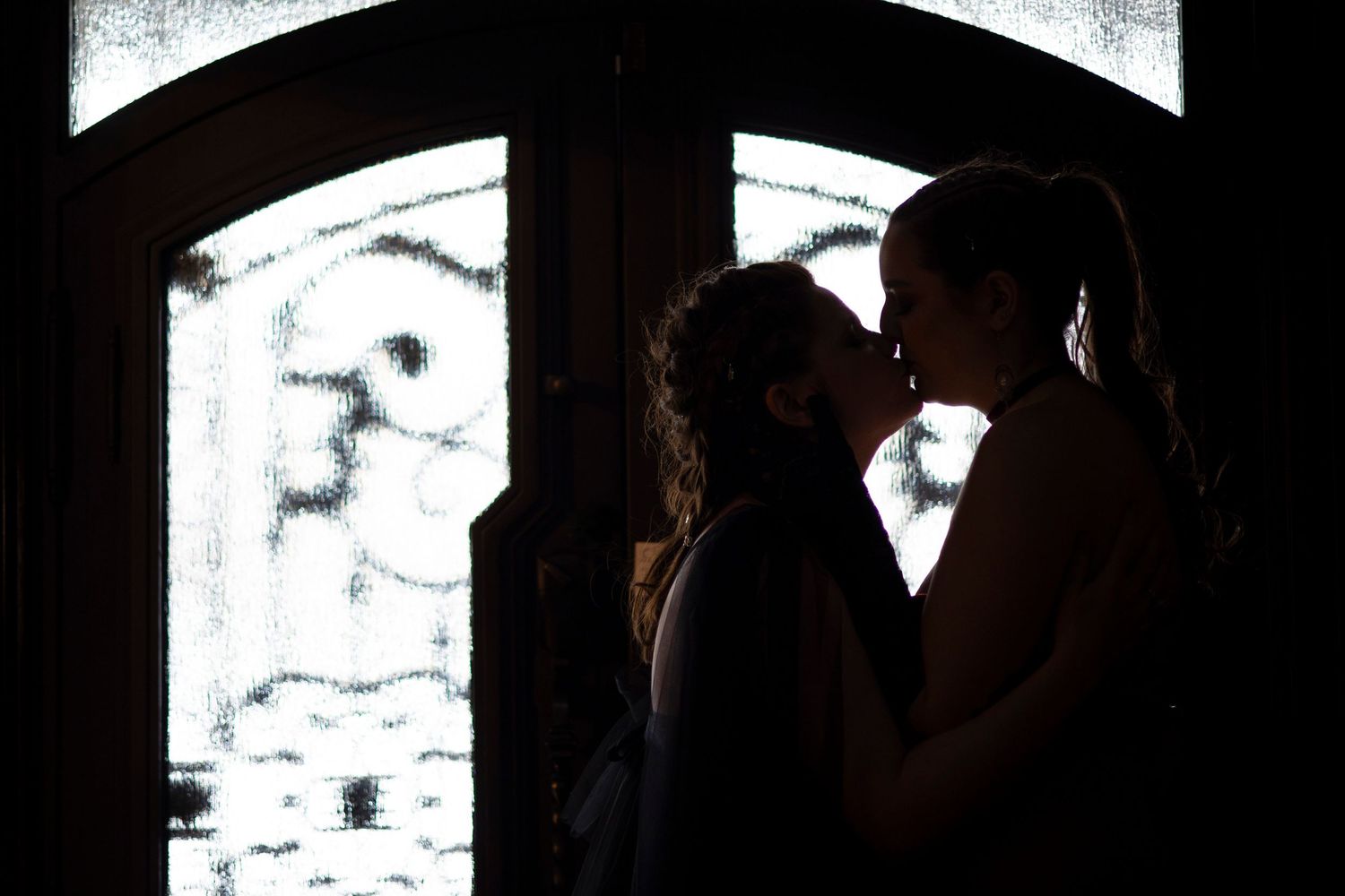 Silhouette of a lesbian couple kissing in front of the front doors of the Satanic Temple in Salem, MA.