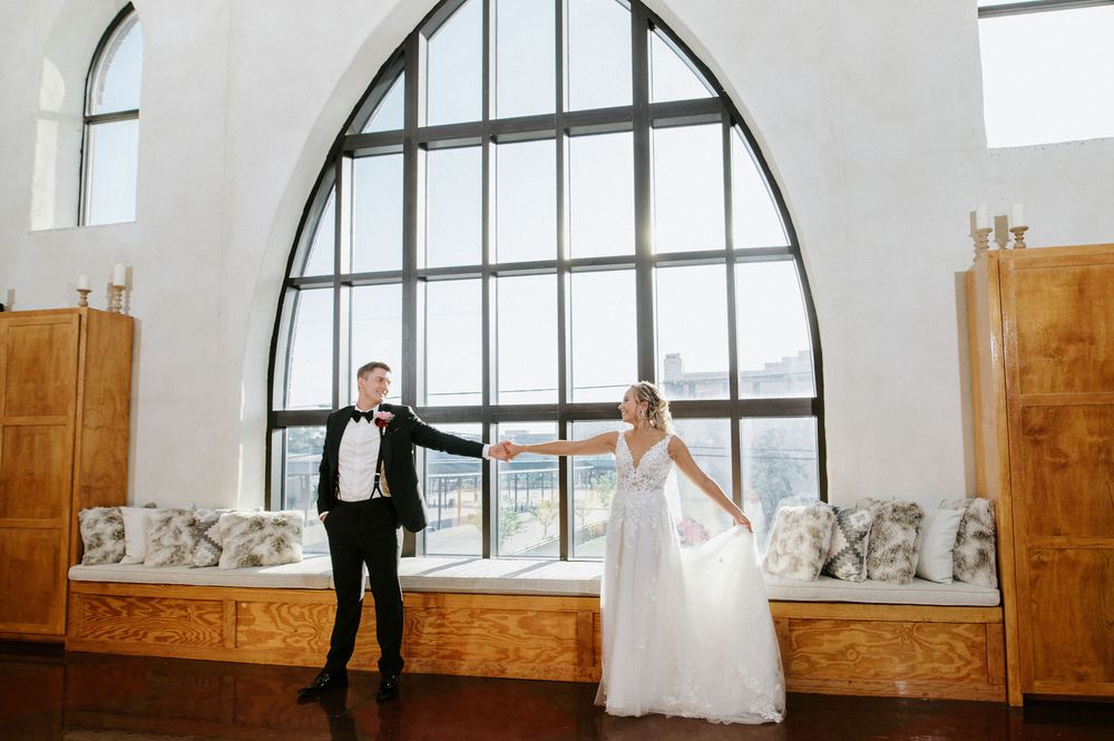 Wedding couple dances together in an elegant venue with arched windows and wooden paneling.