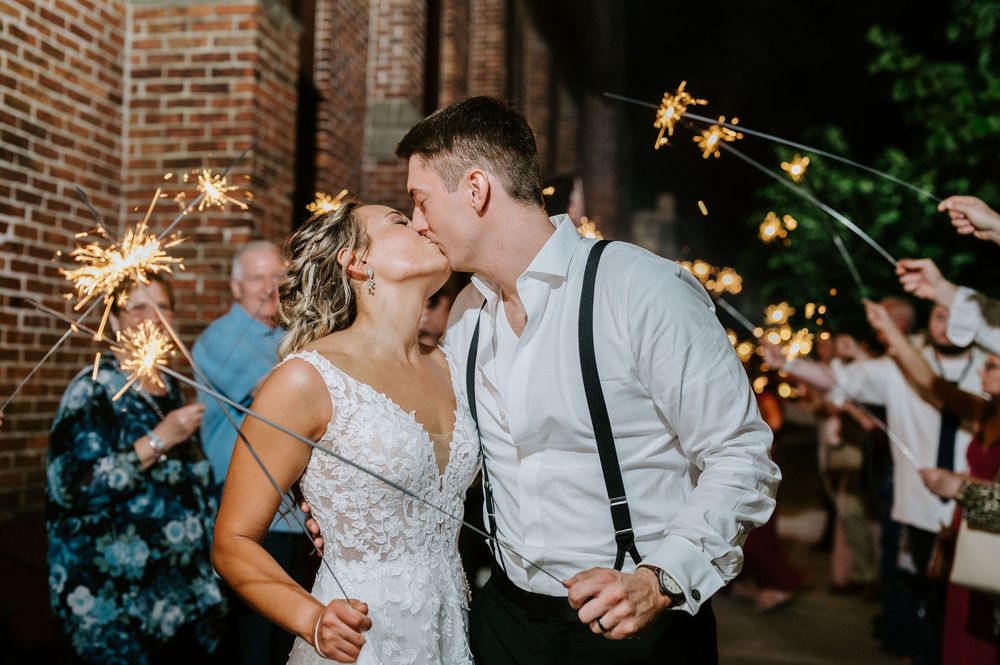 A couple shares a romantic moment at their wedding reception with sparklers glowing in the background.