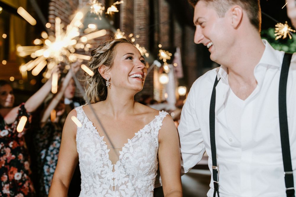Newlywed couple dances and laughs together surrounded by sparklers during their wedding reception celebration.