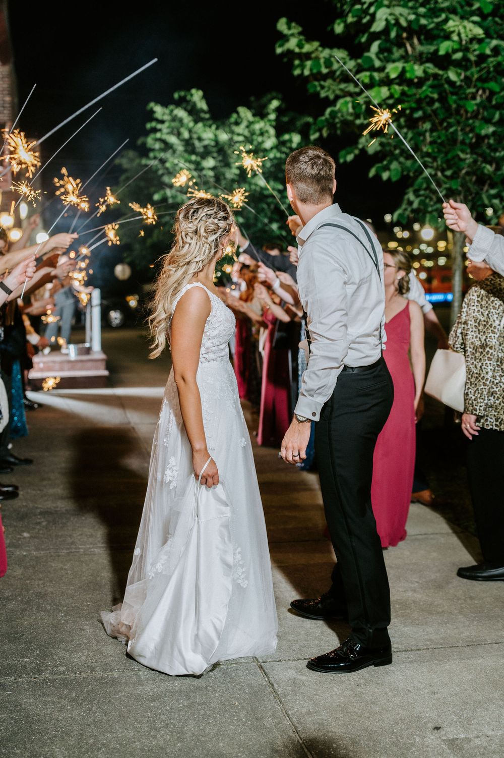 Wedding guests holding sparklers create a magical exit tunnel for the newlyweds on a nighttime celebration.
