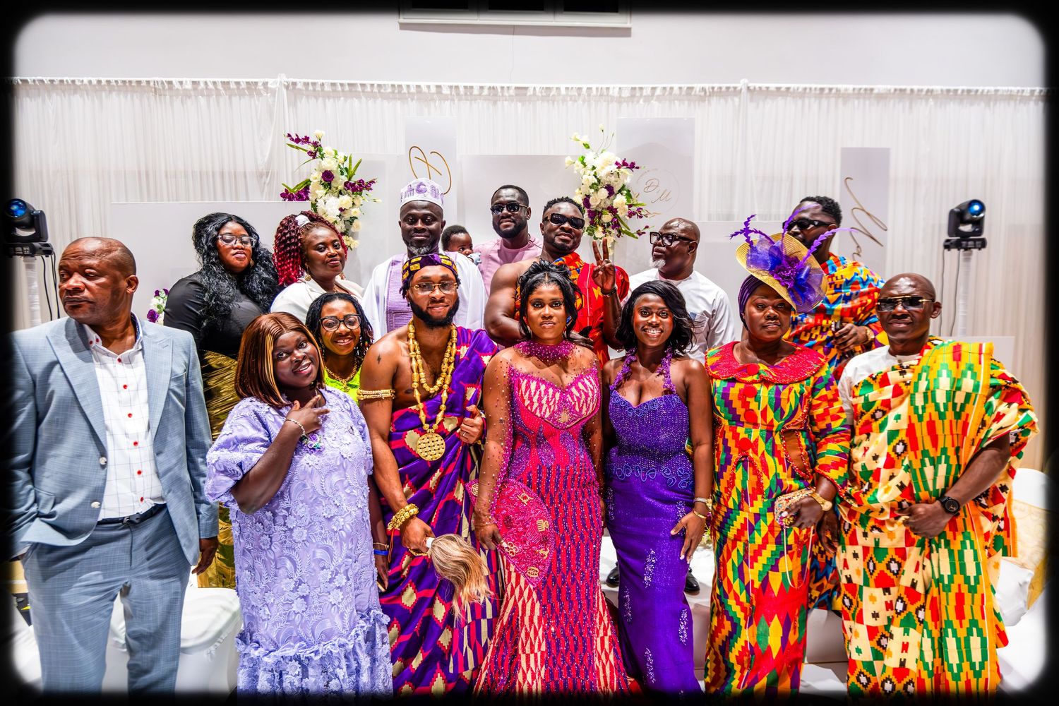 Group of people wearing vibrant traditional African clothing in purple, pink and yellow patterns at a celebration.