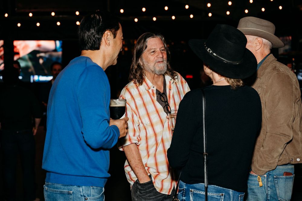 Group of people having an animated conversation at a dimly lit indoor venue.