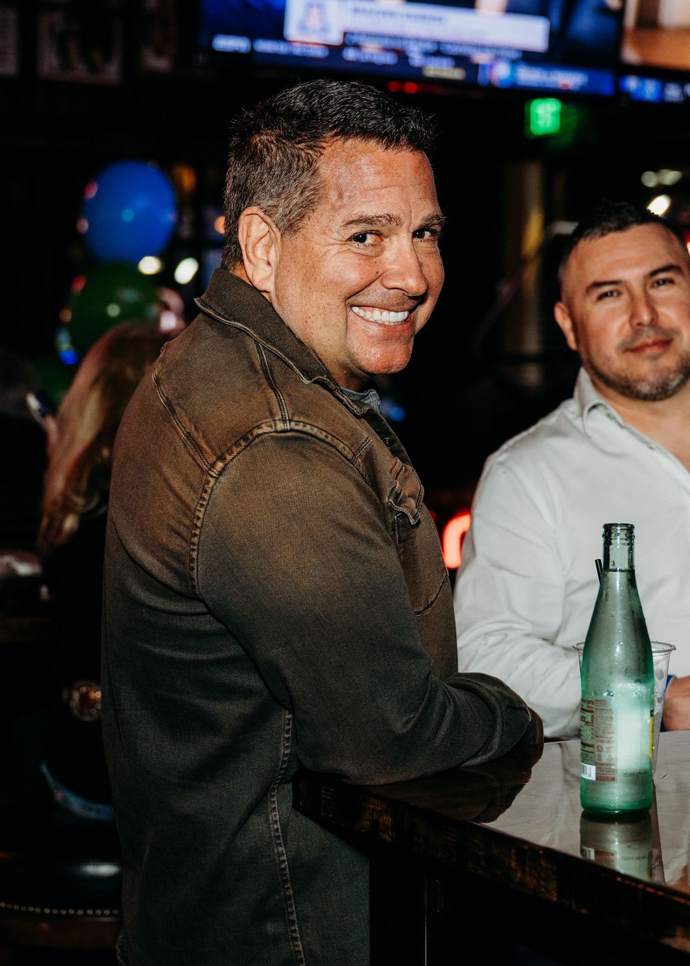 A person in a dark jacket sits at a bar counter with drinks, shown in a sequence of similar poses.