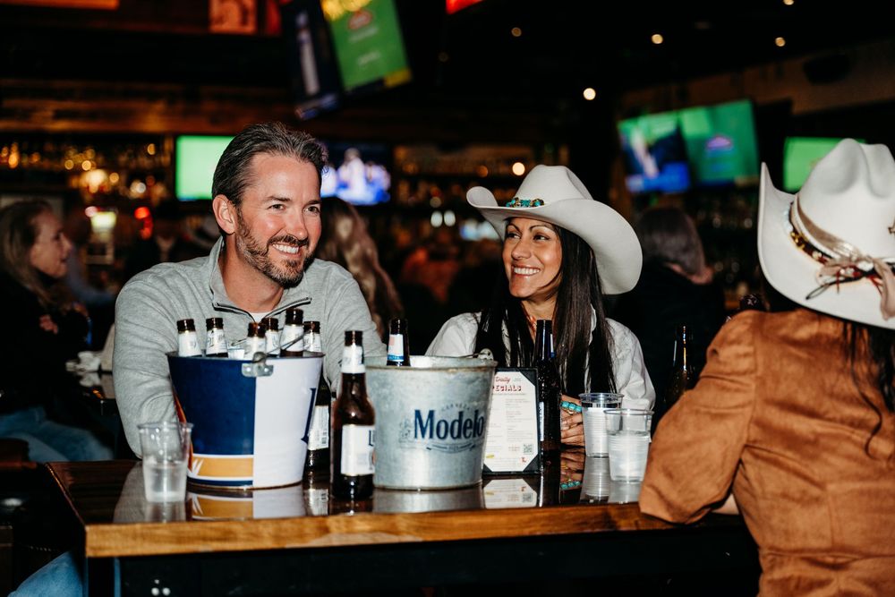 Friends enjoying drinks and conversation at a lively sports bar with TVs in the background.