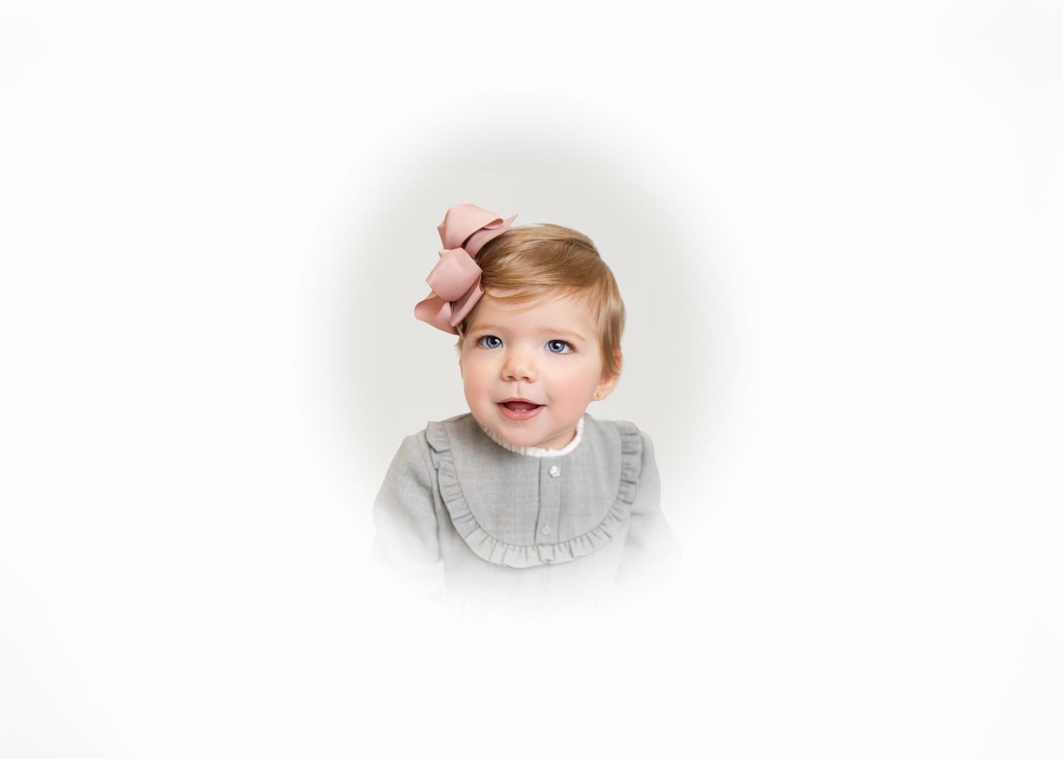 A smiling baby wearing a gray sweater sits against a white background.