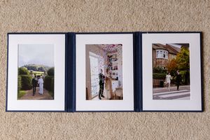 Three framed wedding photographs hanging on a beige wall showing outdoor and indoor ceremony moments.
