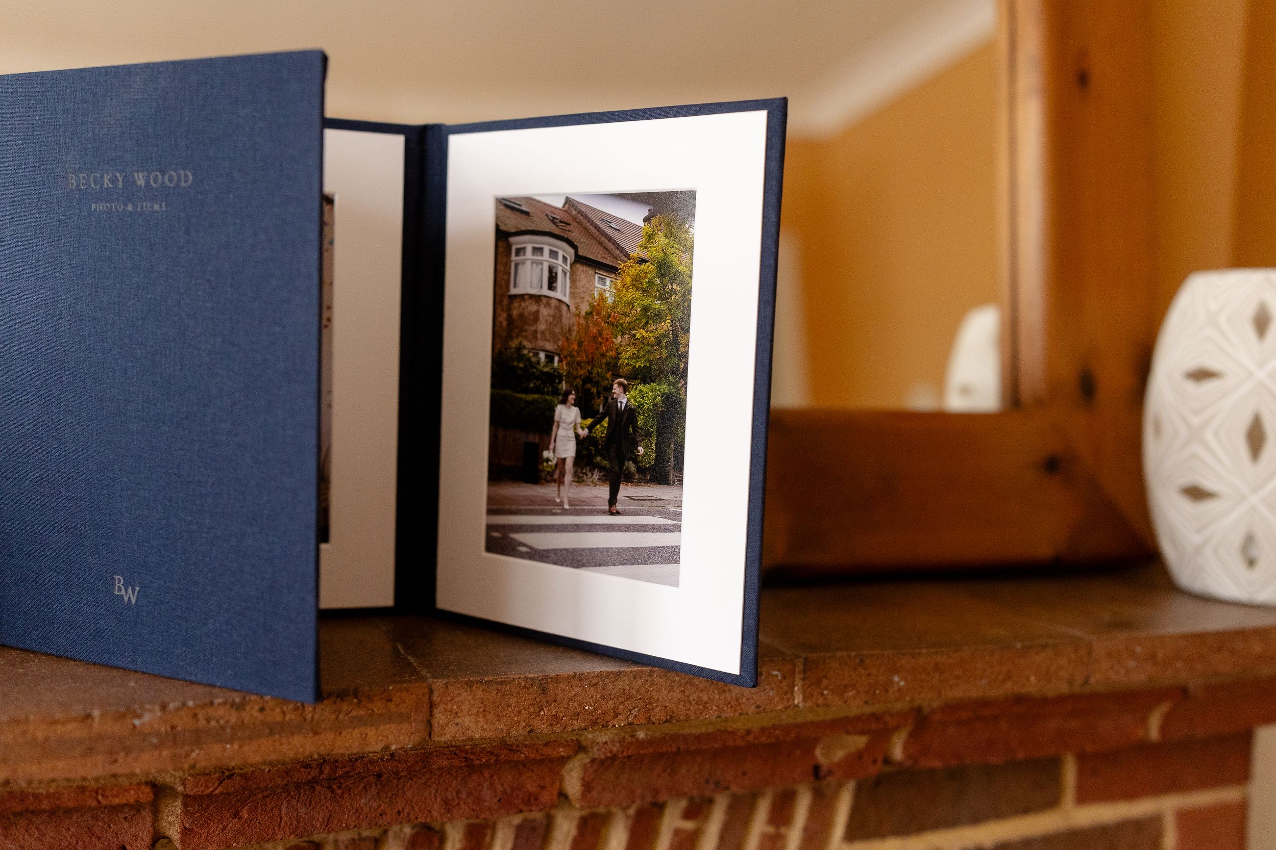 A blue photo album sits open on a wooden shelf, displaying a framed photograph of a house exterior.