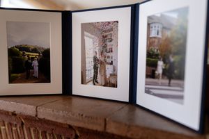 A gallery wall displays a series of framed black and white photographs mounted in a horizontal line against a white wall.