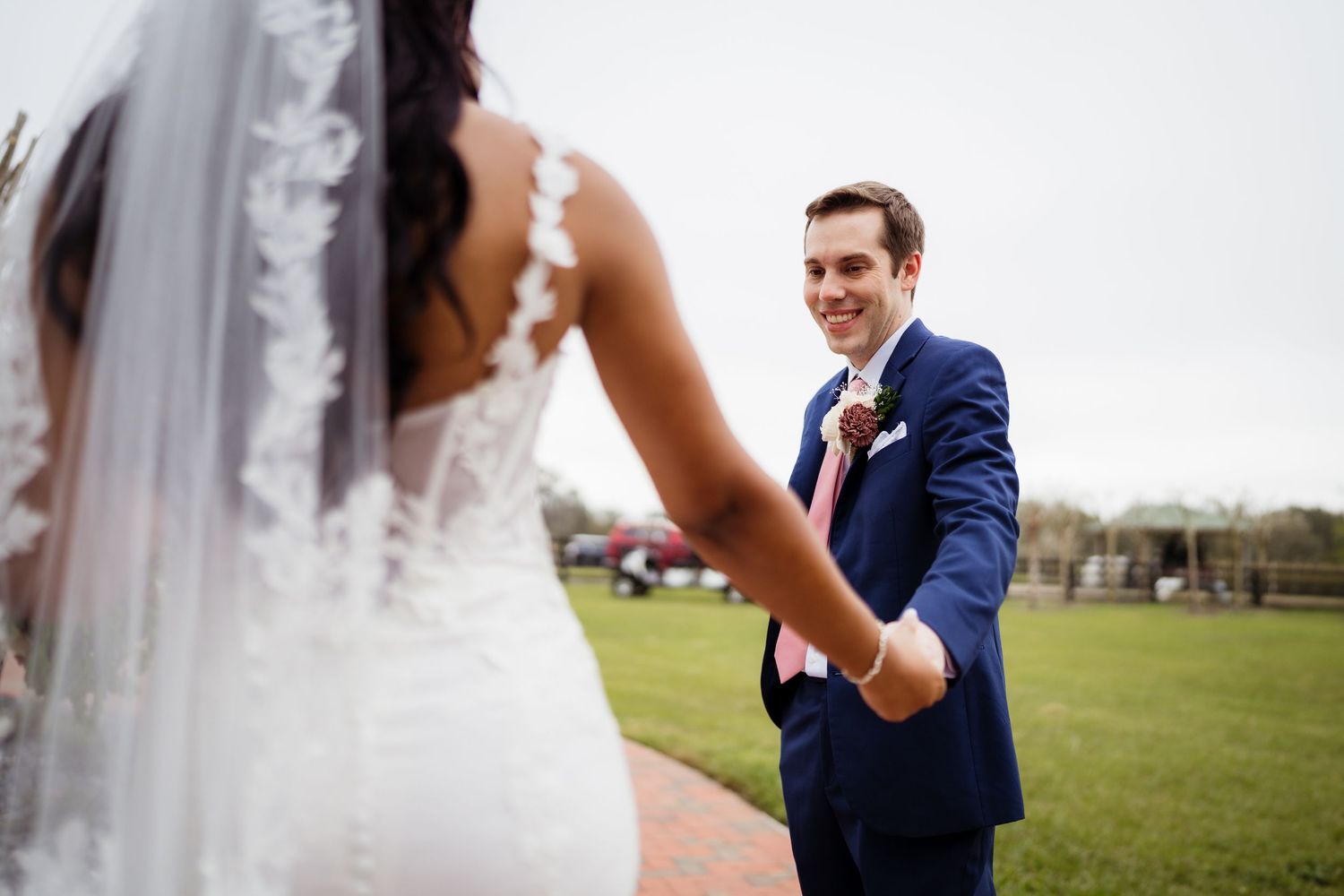 A joyful moment captured between newlyweds on a grassy field, with the bride in white and groom in navy blue.
